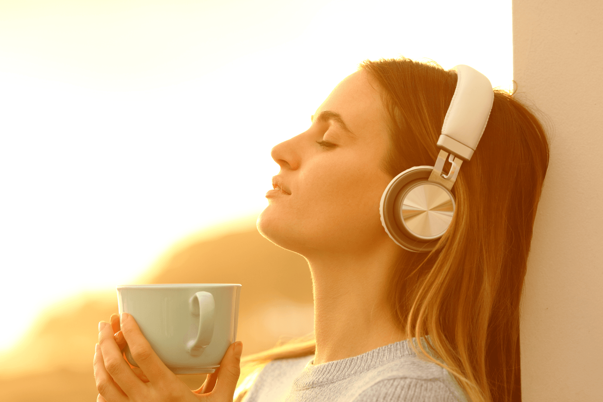 A quiet listener wearing headphones with a warm drink
